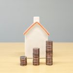 miniature house behind stacked coins