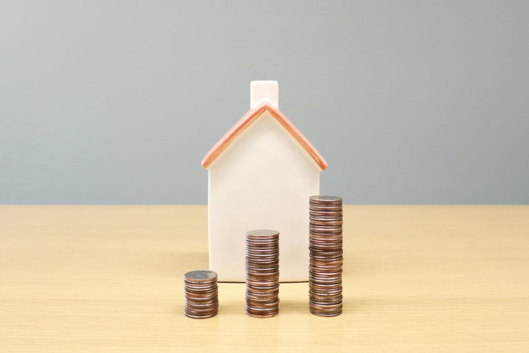 miniature house behind stacked coins