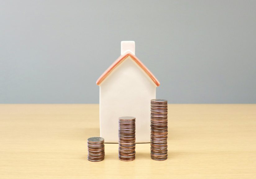 miniature house behind stacked coins