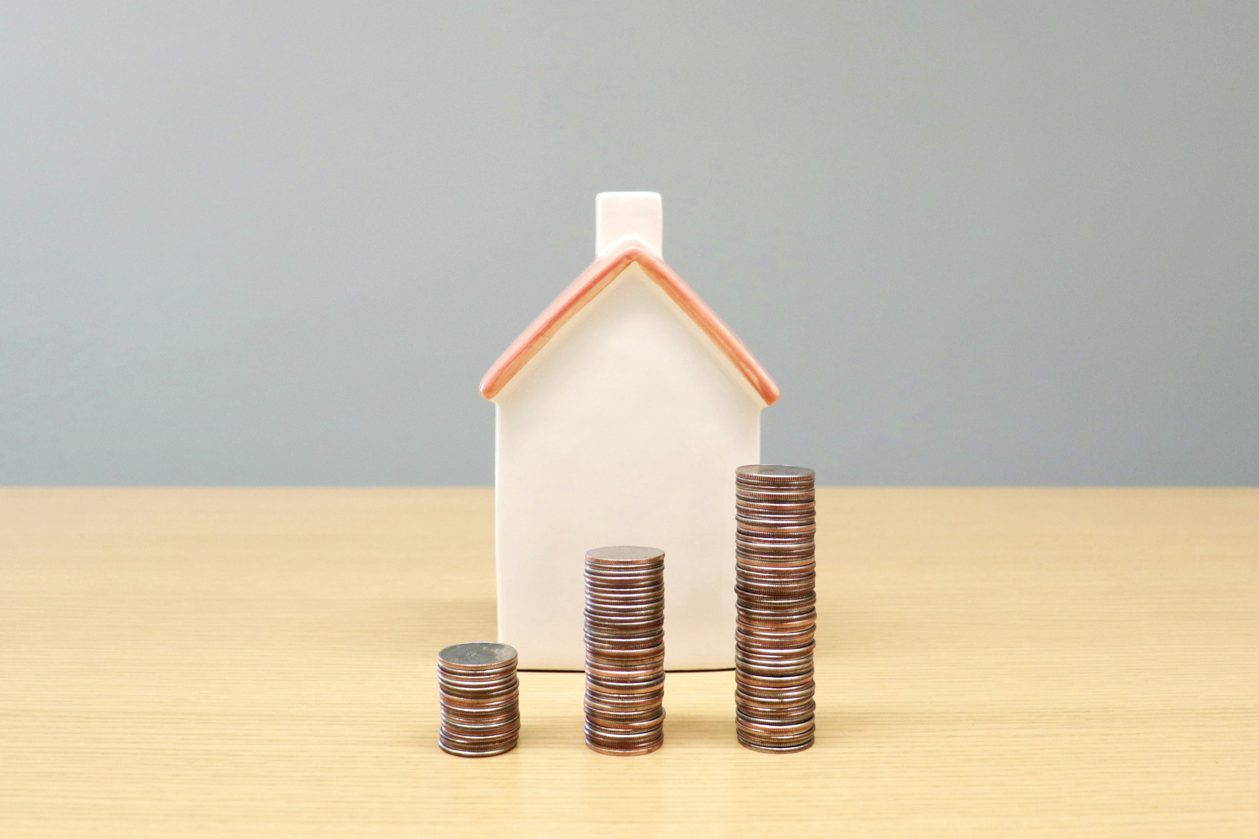 miniature house behind stacked coins