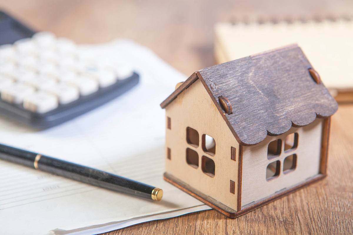 miniature home, calculator, pen, and notepad on a desk